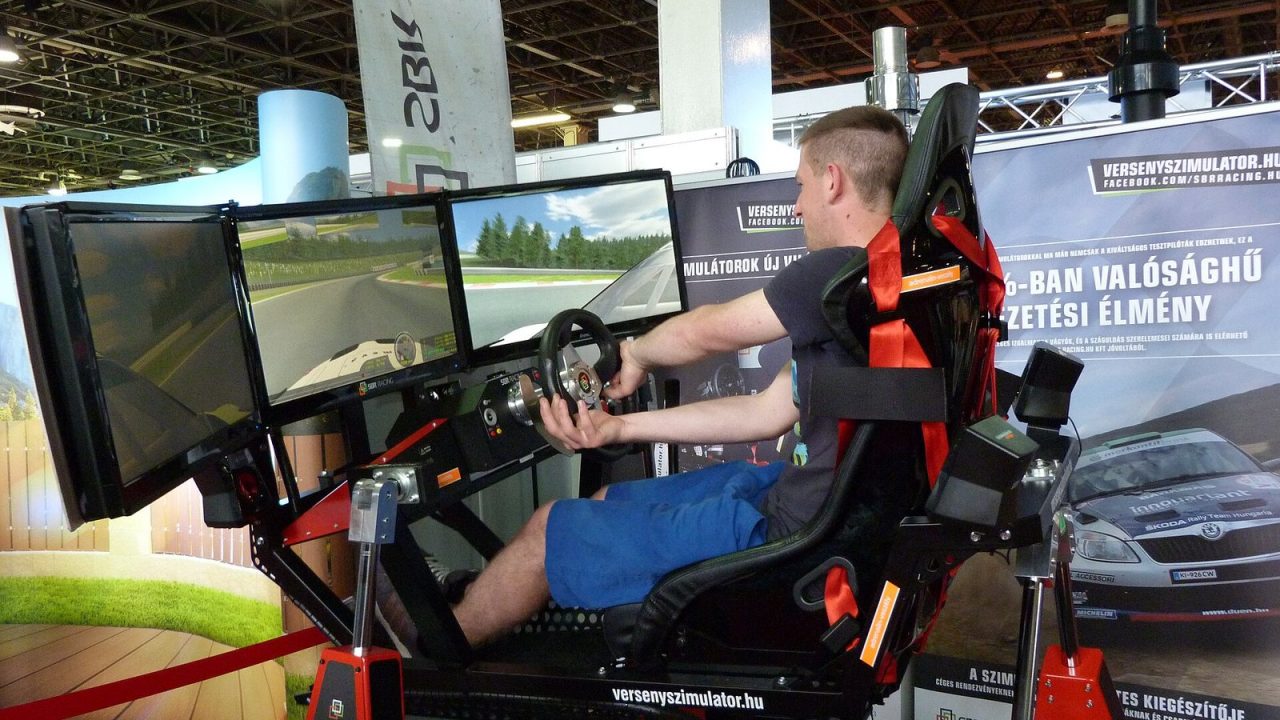 Driver in a racing simulator cockpit with wheel and screens at the Construma exhibition in 2015